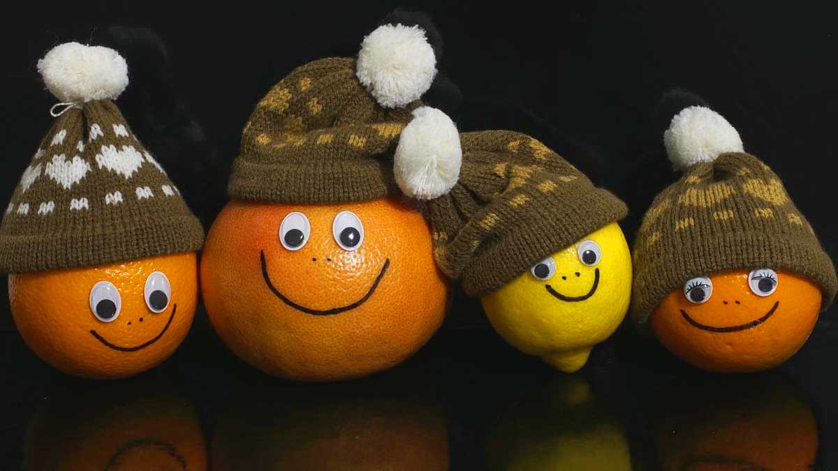 3 oranges et un citron avec des visages souriants vêtus de bonnets en tricot marron.