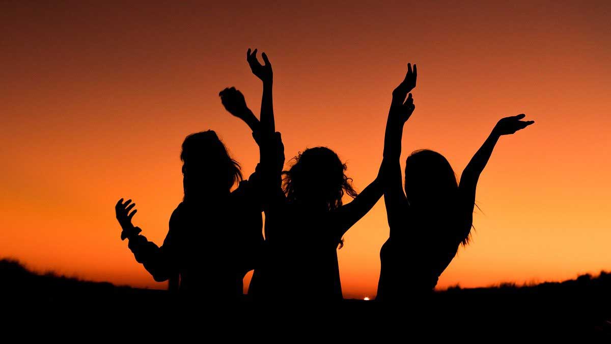 silhouette de 3 femmes heureuses contre le ciel orange.