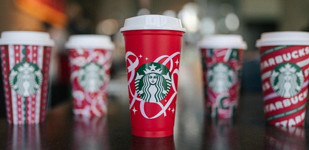 Gambar cangkir liburan Starbucks dari tahun-tahun sebelumnya dengan desain merah, hijau, dan putih yang ceria.