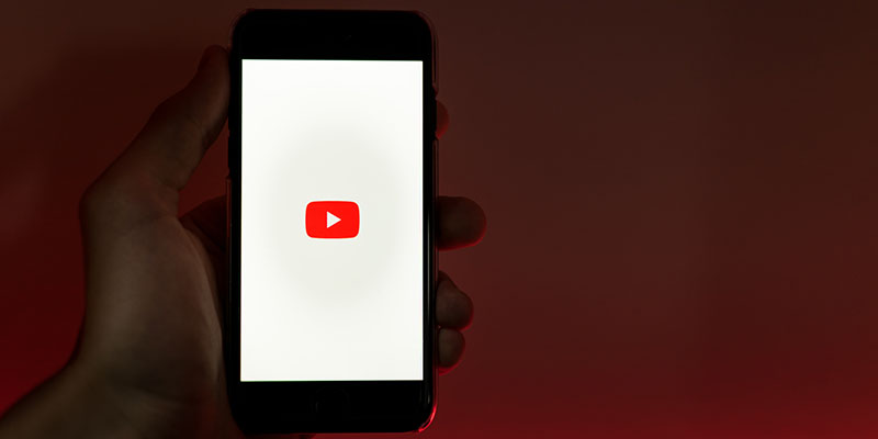 Una mano che tiene un cellulare con il logo di YouTube sullo schermo