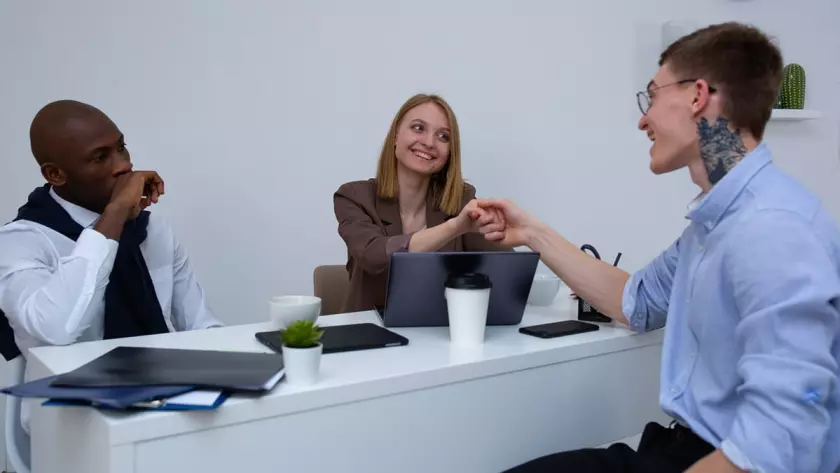 Eine Gruppe von Menschen schüttelt sich an einem Schreibtisch in einem Büro die Hand.