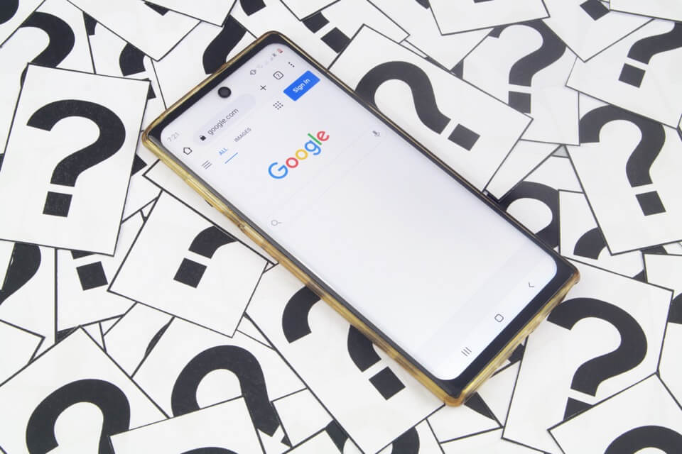 Telefon komórkowy na stronie głównej Google otoczony znakami zapytania