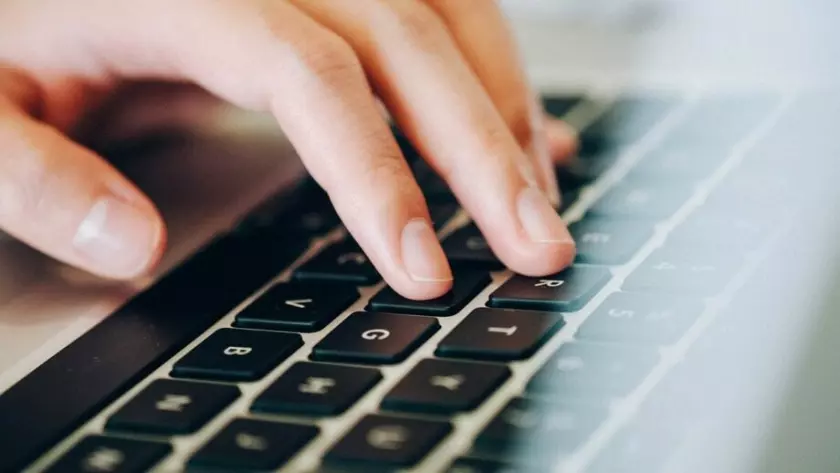 A mão de uma pessoa está digitando em um teclado de laptop.