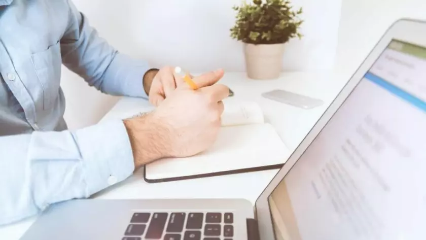 Um homem sentado em uma mesa com um laptop, um caderno e uma caneta.