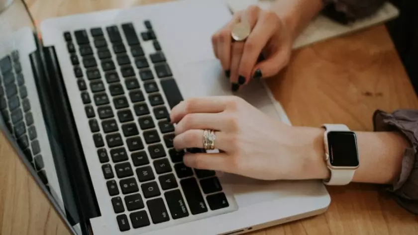 Eine Frau tippt mit einer Apple Watch auf einem Laptop.