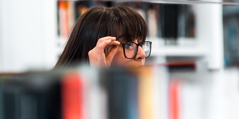 図書館で本をチェックする黒いスペックを着た女性